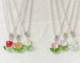Puede incluir: Conjunto de cinco collares de cadena plateada con colgantes en forma de tulipán. Los tulipanes están hechos de vidrio y vienen en cinco colores diferentes: rojo, naranja, amarillo, rosa y verde.