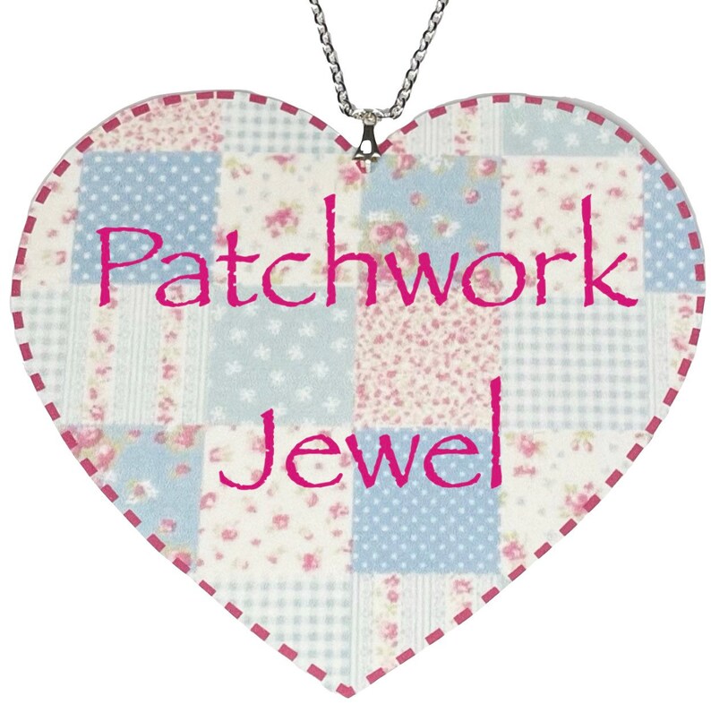 Puede incluir: Un adorno de tela de forma de coraz&oacute;n con una cadena plateada. La tela es una mezcla de patrones florales azules y rosas. Las palabras "Patchwork Jewel" est&aacute;n escritas en rosa en el adorno.