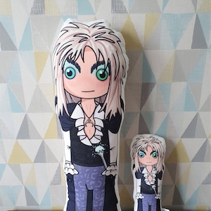 May include: Two plush pillows featuring a cartoon character with long blonde hair, a black and white outfit, and a blue and white wand. The larger pillow is about 18 inches tall and the smaller pillow is about 12 inches tall.
