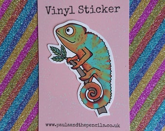 May include: A vinyl sticker featuring a cartoon chameleon with orange, blue, and green colors. The chameleon is perched on a branch with leaves. The sticker says "Vinyl Sticker" at the top and "www.paulaandthepencils.co.uk" at the bottom.