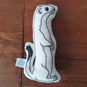 May include: White plush toy shaped like a weasel with black eyes and a black tail. The toy is standing upright and has a tag that says "Pilla & the Priscilla".