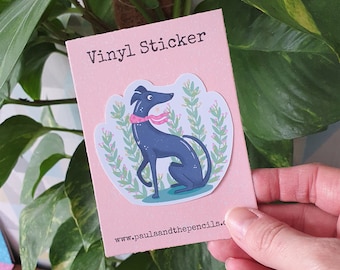 May include: Vinyl sticker featuring a black and white illustration of a dog wearing a pink collar, surrounded by green foliage with pink flowers. The sticker is on a pink background with the text "Vinyl Sticker" and "www.paulaandthepencils.co.uk".