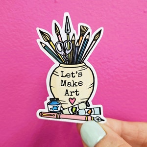 May include: A sticker featuring a white ceramic jar with the text "Let's Make Art" and a pink heart. The jar is filled with various art supplies, including paintbrushes, pencils, a pair of scissors, and a paint tube.