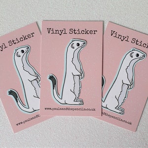 May include: Three pink cards with the text "Vinyl Sticker" printed on them. Each card features a white cartoon weasel with black eyes and a black tail. The text "www.paulaandthepencils.co.uk" is printed on the bottom of each card.
