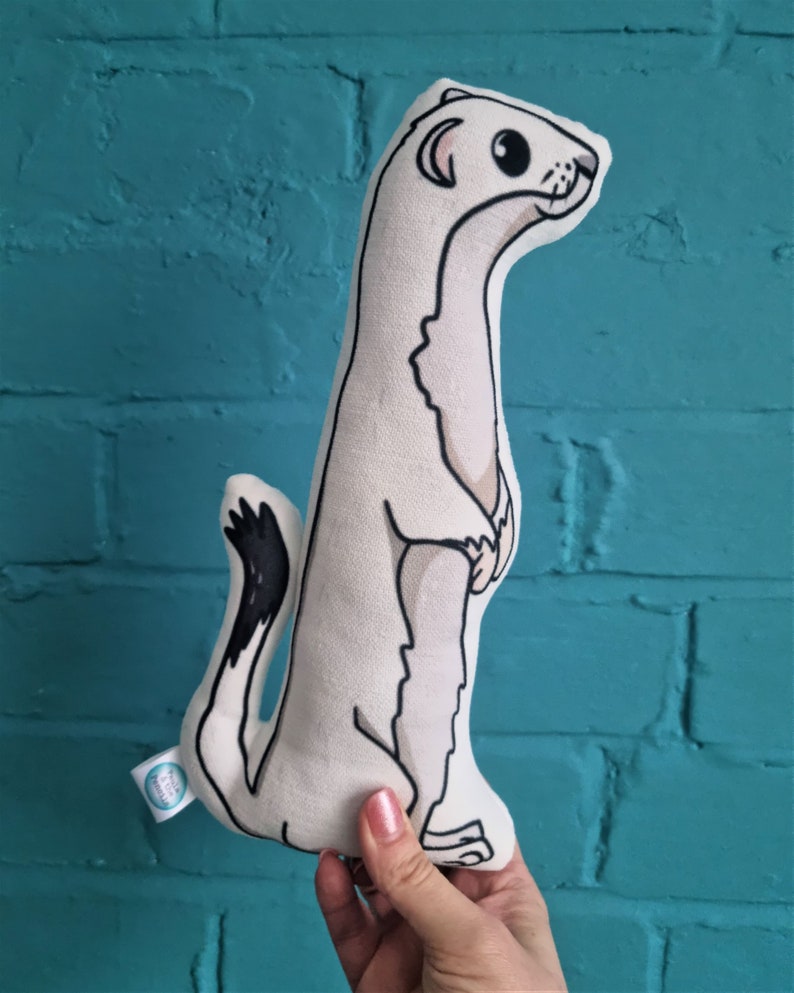 May include: A white plush toy shaped like a weasel standing on its hind legs. The toy has black eyes, a black nose, and a black tail.