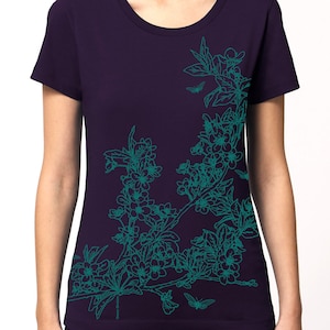 May include: A purple t-shirt with a teal floral design on the right side. The design features a branch with leaves and flowers.
