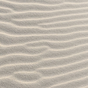 May include: Close-up of white sand with a rippled texture created by the wind.
