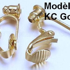May include: Two gold-toned metal clip-on earring converters with a hinged mechanism and a textured base. The components feature a smooth, polished finish and include the text Mod&egrave;le 1 KC Gold printed in black on the upper right side of the image.