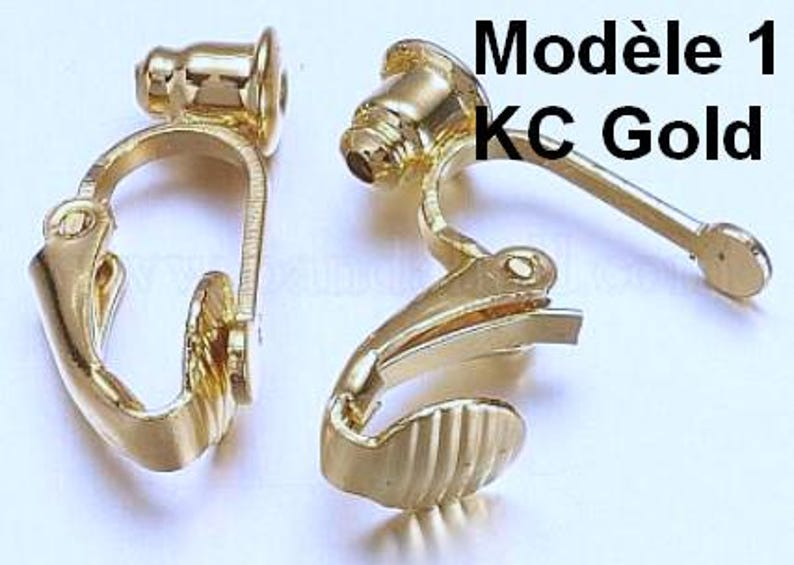 May include: Two gold-toned metal clip-on earring converters with a hinged mechanism and a textured base. The components feature a smooth, polished finish and include the text Mod&egrave;le 1 KC Gold printed in black on the upper right side of the image.