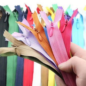Könnte beinhalten: Eine Sammlung mehrerer Nylon-Reißverschlüsse in verschiedenen leuchtenden Farben wie Pink, Orange, Lavendel, Beige, Rot, Blau, Grün und Schwarz. Jeder Reißverschluss verfügt über einen passenden Schiebergriff und ein gewebtes Stoffband.