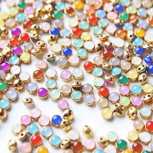 Può includere: Una collezione di perline rotonde colorate in pietre preziose con montature in metallo color oro. Le perline sono di vari colori, tra cui rosso, blu, verde, viola e bianco. Queste piccole perline sono ideali per la creazione di gioielli e l'artigianato.