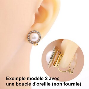 May include: A gold-toned clip-on earring featuring a central white pearl surrounded by a circular border of small clear crystals. The earring mechanism is visible in a circular inset, showing a gold metal hinge with a clear plastic pad.