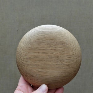 Könnte beinhalten: Ein rundes Holzobjekt in hellem Braun mit strukturierter Oberfläche. Das Objekt wird in einer Hand gehalten und scheint ein dekoratives Element oder Teil eines größeren Stücks zu sein. Die Holzmaserung ist sichtbar.