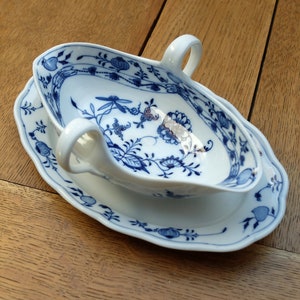 Könnte beinhalten: Eine weiße Porzellansauce mit einem blauen und weißen Blumenmuster. Die Sauce hat zwei Griffe und steht auf einer passenden Untertasse.