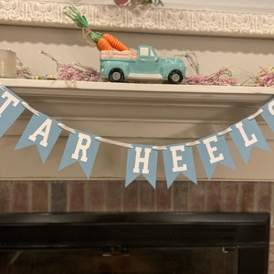 K&ouml;nnte beinhalten: Ein blaues und wei&szlig;es Banner mit dem Text "TAR HEELS" h&auml;ngt &uuml;ber einem Kamin.