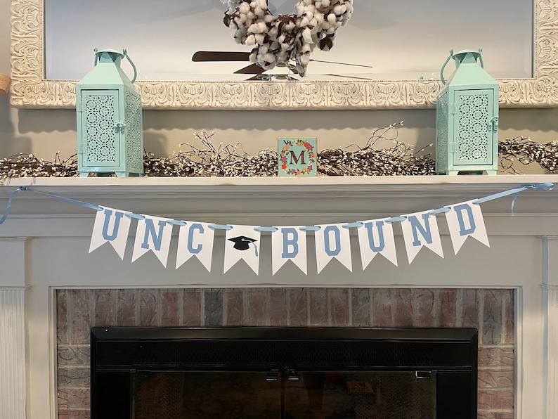 K&ouml;nnte beinhalten: Ein wei&szlig;-blaues Banner mit dem Text "UNC BOUND" h&auml;ngt an einem wei&szlig;en Kaminsims. Das Banner hat ein Abschlusskappen-Symbol anstelle des Buchstabens "C".