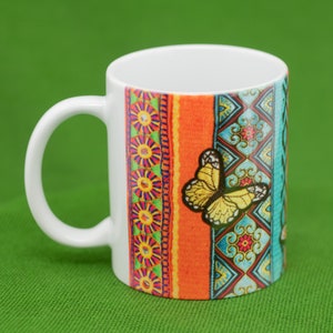 May include: White ceramic mug with a colorful design featuring a butterfly and geometric patterns. The mug has a handle and is perfect for hot beverages.