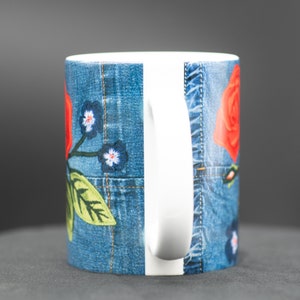May include: A white ceramic mug with a denim-inspired design featuring red roses and blue flowers. The mug has a white handle.