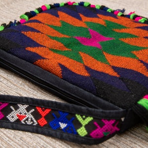 May include: A colorful woven bag with a geometric pattern in shades of orange, green, blue, and black. The bag has a zipper closure and a long strap with embroidered details.