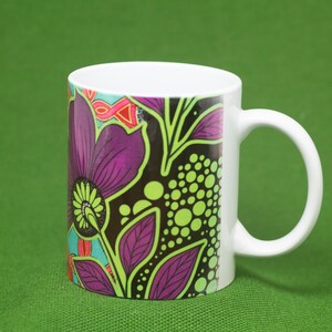 Pode incluir: Uma caneca de cer&acirc;mica branca com um design floral colorido. O design apresenta flores e folhas roxas, verdes e pretas sobre um fundo preto.