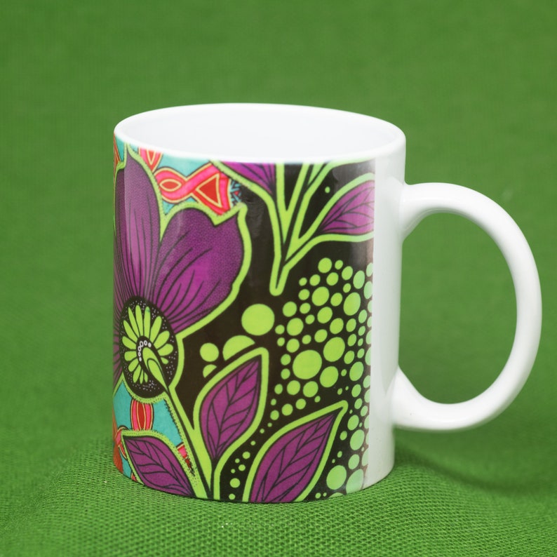 Pode incluir: Uma caneca de cer&acirc;mica branca com um design floral colorido. O design apresenta flores e folhas roxas, verdes e pretas sobre um fundo preto.