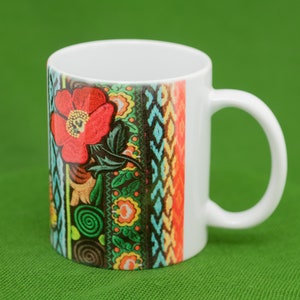 May include: White ceramic mug with a colorful floral design featuring a red flower and green leaves. The design includes a variety of colorful stripes and patterns.
