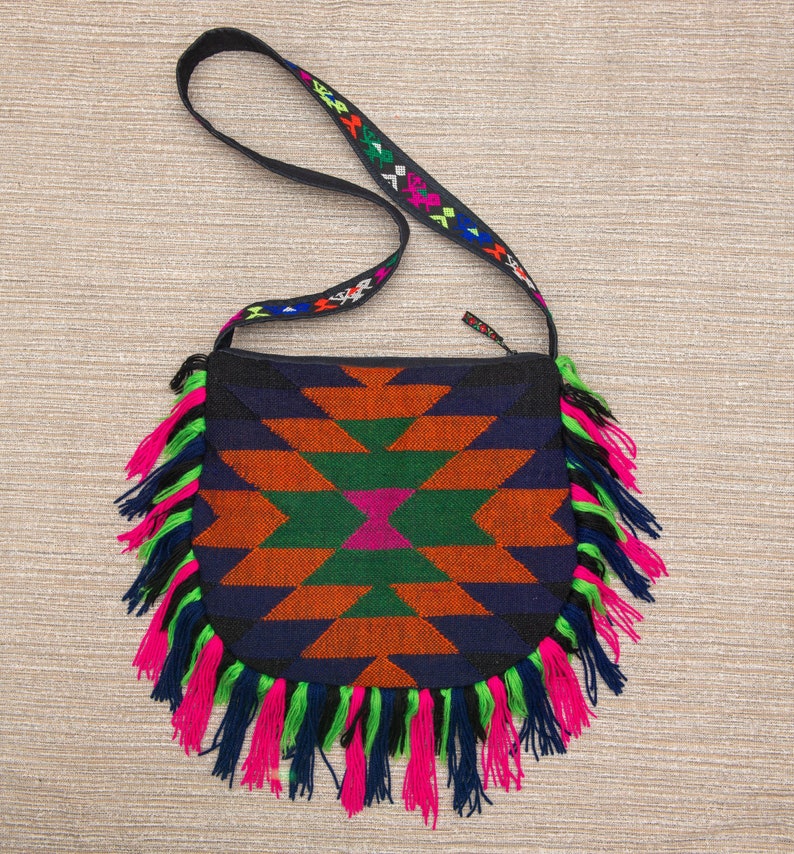May include: A black and blue crossbody bag with a geometric pattern and fringe trim. The bag has a black strap with colorful embroidery.