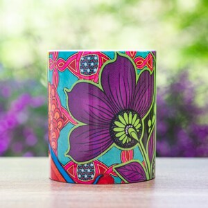 Pode incluir: Uma caneca de cer&acirc;mica colorida com um design floral. A caneca apresenta uma grande flor roxa com detalhes verdes e um fundo azul. O design &eacute; intrincado e detalhado.