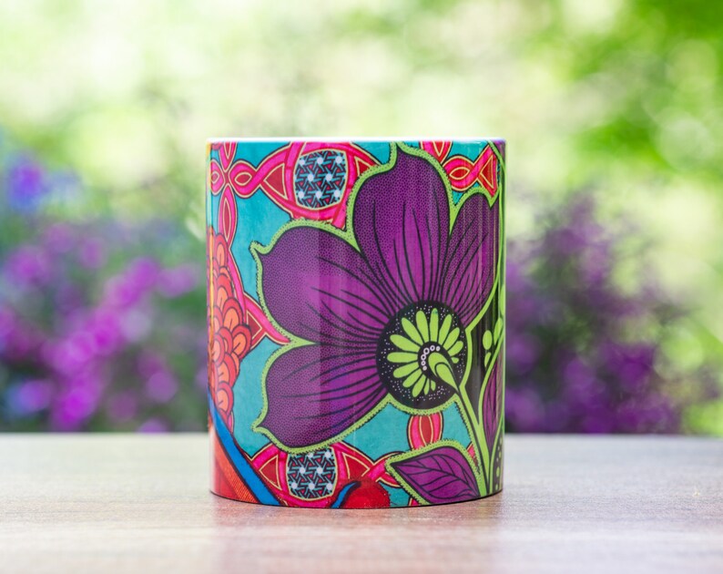 Pode incluir: Uma caneca de cer&acirc;mica colorida com um design floral. A caneca apresenta uma grande flor roxa com detalhes verdes e um fundo azul. O design &eacute; intrincado e detalhado.