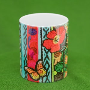 May include: A white ceramic mug with a colorful design featuring a butterfly, flowers, and geometric patterns. The design is reminiscent of traditional Mexican embroidery.