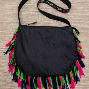 May include: Black crossbody bag with a long strap and fringe trim in pink, green, and blue.