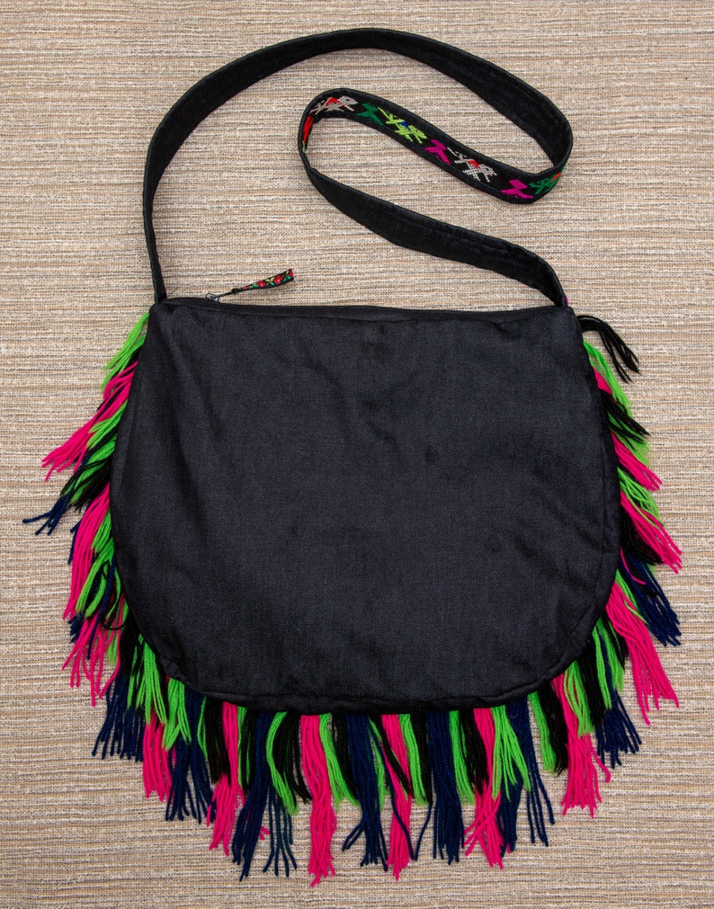 May include: Black crossbody bag with a long strap and fringe trim in pink, green, and blue.