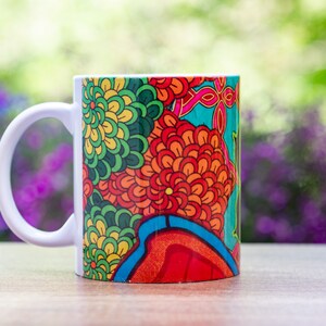 Pode incluir: Uma caneca de cer&acirc;mica branca com um design floral colorido. O design apresenta flores vermelhas, laranja, amarelas, verdes, azuis e roxas.