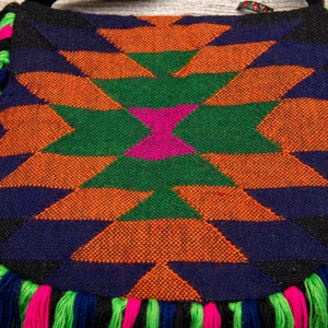 May include: A colorful woven bag with a geometric pattern in shades of orange, green, pink, blue, and black. The bag has a fringe border in pink, green, and blue.