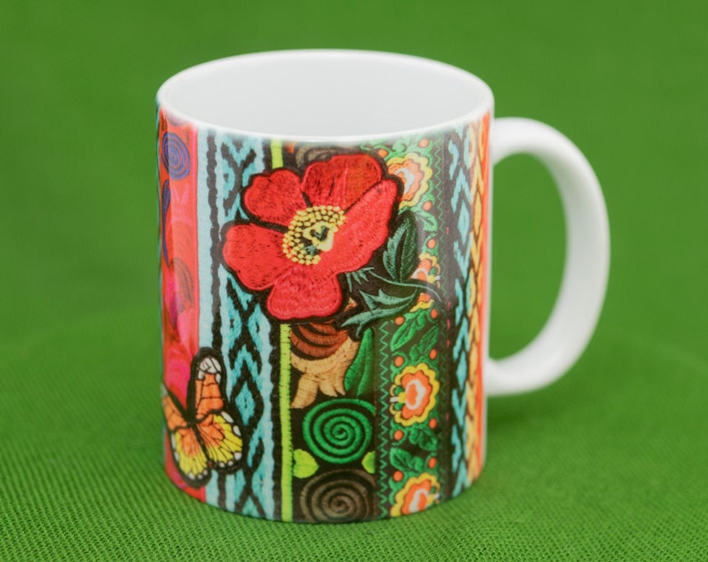May include: A white ceramic mug with a colorful floral design. The design features a red flower with green leaves, a butterfly, and a variety of colorful stripes and patterns.
