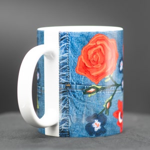 May include: White ceramic mug with a blue denim pattern and red, orange, and blue floral embroidery.