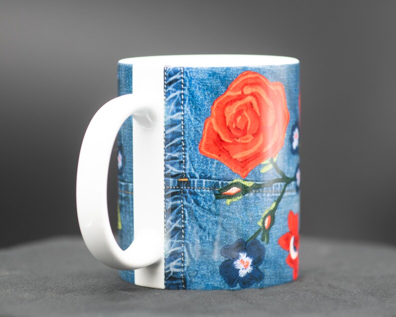 May include: White ceramic mug with a blue denim pattern and red, orange, and blue floral embroidery.