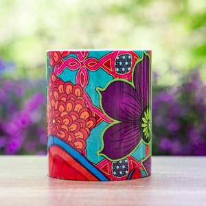 Pode incluir: Uma caneca de cer&acirc;mica colorida com um design floral em vermelho, laranja, roxo, azul e verde. A caneca est&aacute; sobre uma superf&iacute;cie de madeira.