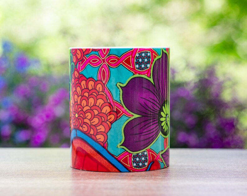 Pode incluir: Uma caneca de cer&acirc;mica colorida com um design floral em vermelho, laranja, roxo, azul e verde. A caneca est&aacute; sobre uma superf&iacute;cie de madeira.