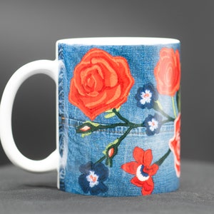 May include: White ceramic mug with a blue denim pattern and red, orange, and blue embroidered flowers.