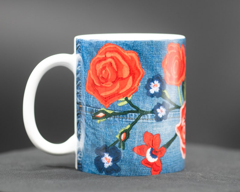 May include: White ceramic mug with a blue denim pattern and red, orange, and blue embroidered flowers.