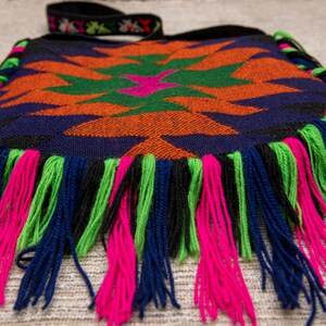 May include: A colorful woven bag with a geometric pattern and fringe trim in shades of blue, green, orange, pink, and black.