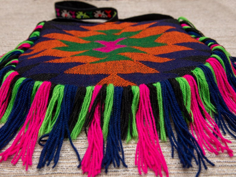 May include: A colorful woven bag with a geometric pattern and fringe trim in shades of blue, green, orange, pink, and black.