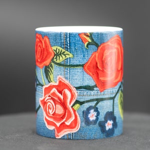 May include: A blue ceramic mug with a denim pattern and red roses embroidered on it.