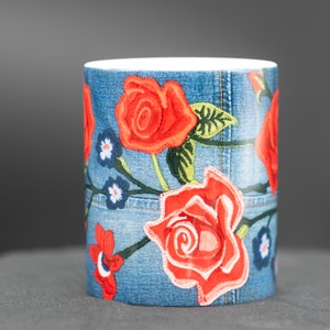 May include: A white ceramic mug with a blue denim pattern and red embroidered roses.