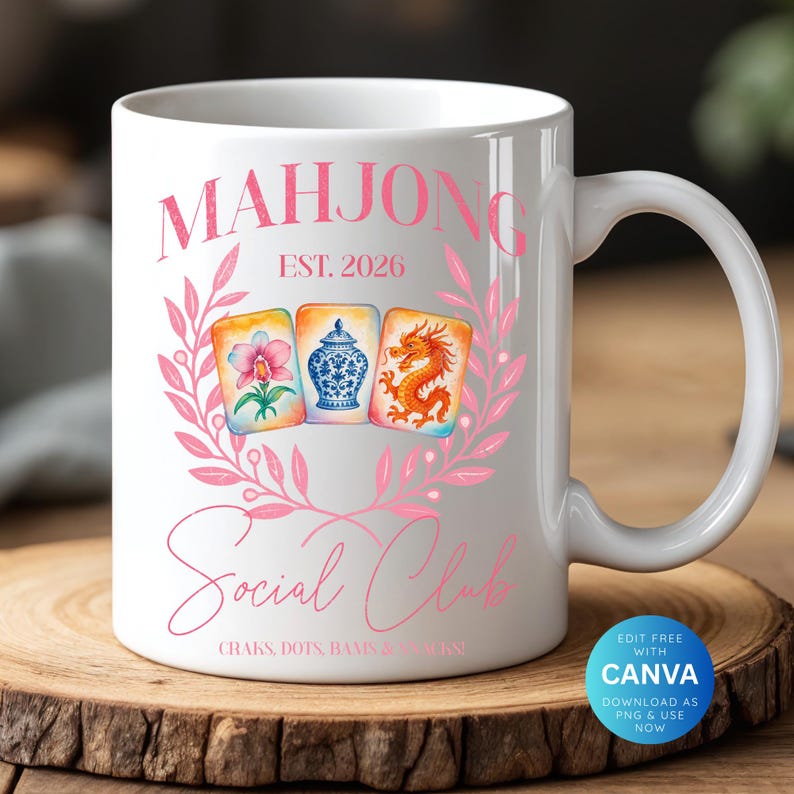 May include: White ceramic mug featuring the words "MAHJONG Social Club" in pink script, with "EST. 2026" above. The design includes a pink floral wreath and watercolor illustrations of Mahjong tiles. The mug sits on a wooden surface.