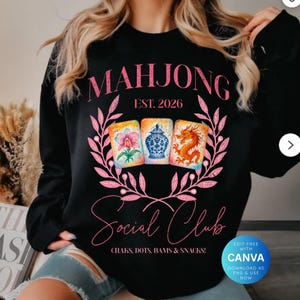 May include: Black sweatshirt with a pink floral design and the words "MAHJONG Social Club" in pink script. The design includes three illustrated Mahjong tiles and the text "EST. 2026". The bottom of the design reads "CRAKS, DOTS, BAMS & SNACKS!"