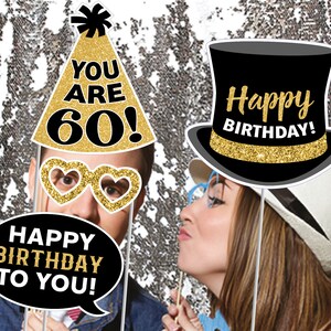Puede incluir: Un conjunto de seis accesorios para cabina de fotos para una fiesta de cumplea&ntilde;os n&uacute;mero 60. Los accesorios incluyen un sombrero de copa negro con purpurina dorada y el texto "&iexcl;Feliz cumplea&ntilde;os!" un gorro de fiesta con purpurina dorada y el texto "&iexcl;Tienes 60 a&ntilde;os!" un globo de di&aacute;logo con el texto "&iexcl;Feliz cumplea&ntilde;os para ti!" y un par de gafas en forma de coraz&oacute;n con purpurina dorada.