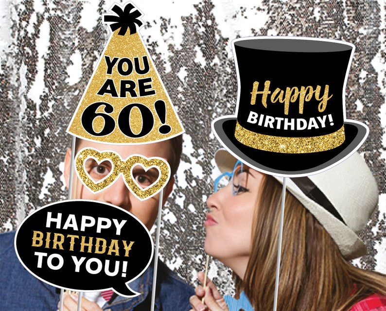 Puede incluir: Un conjunto de seis accesorios para cabina de fotos para una fiesta de cumplea&ntilde;os n&uacute;mero 60. Los accesorios incluyen un sombrero de copa negro con purpurina dorada y el texto "&iexcl;Feliz cumplea&ntilde;os!" un gorro de fiesta con purpurina dorada y el texto "&iexcl;Tienes 60 a&ntilde;os!" un globo de di&aacute;logo con el texto "&iexcl;Feliz cumplea&ntilde;os para ti!" y un par de gafas en forma de coraz&oacute;n con purpurina dorada.