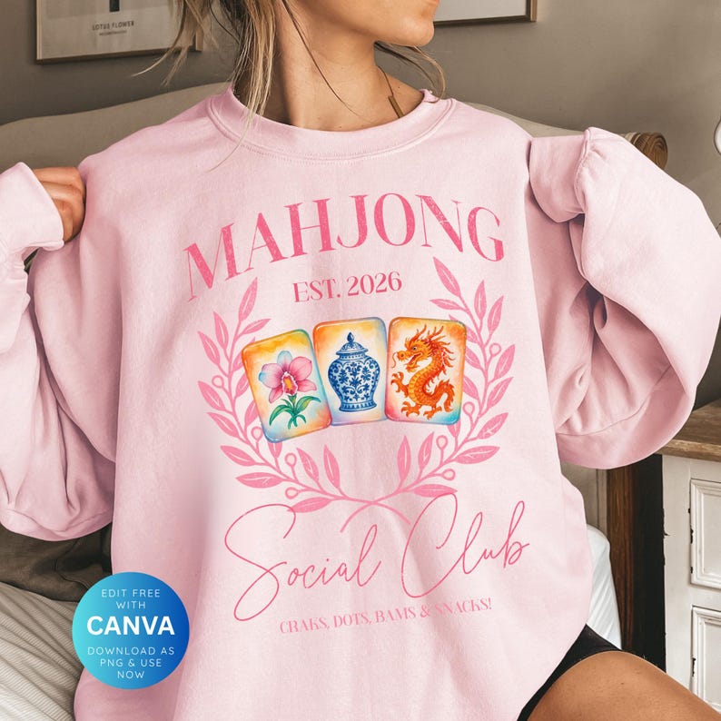May include: A light pink sweatshirt with the word "MAHJONG" in pink script above a wreath design. Below the wreath are three illustrated tiles and the words "Social Club". The text "EST. 2026" is above the tiles. The sweatshirt has long sleeves.